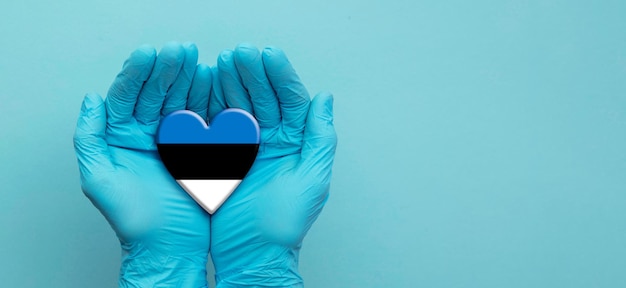 Manos de los médicos con guantes quirúrgicos sosteniendo el corazón de la bandera de Estonia