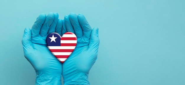 Foto manos de los médicos con guantes quirúrgicos sosteniendo el corazón de la bandera de liberia