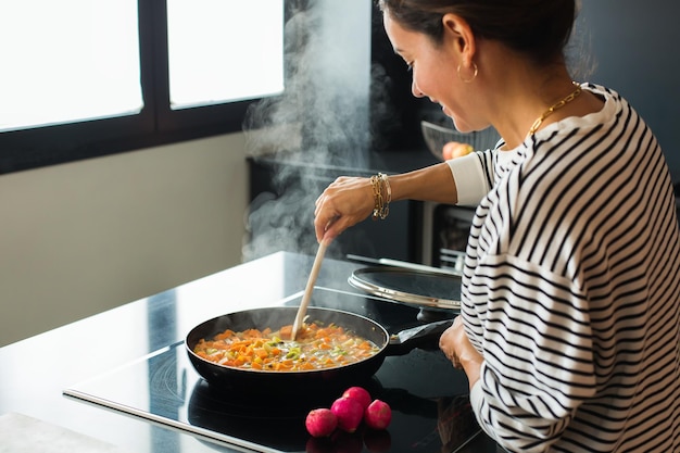 Manos de mujer agregando ingredientes en un guiso de verduras