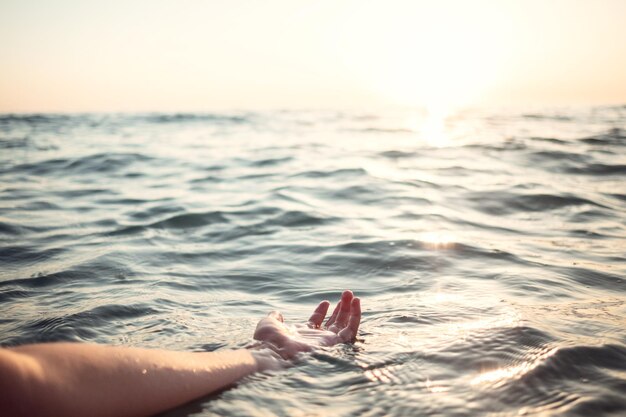 Manos de mujer en el agua invitándote sobre los rayos dorados del atardecer