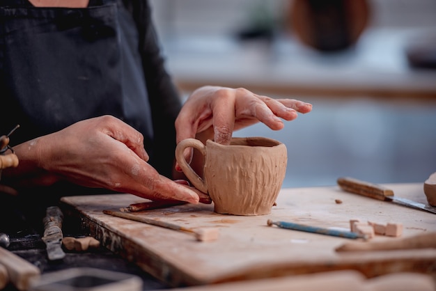 Manos de mujer alfarero formando taza de arcilla