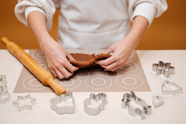 Manos de mujer amasando masa de pan de jengibre para hacer pan de jengibre navideño con moldes de metal para confección ...