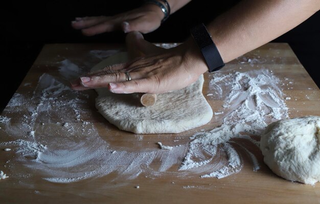 Las manos de la mujer amassando masa fresca para hacer pan o pizza en una mesa de harina