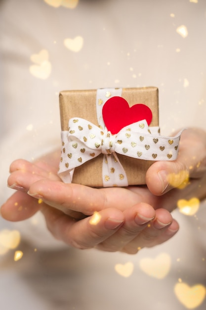 Manos de mujer de belleza sosteniendo caja de regalo con corazón rojo sobre rosa resplandor bokeh