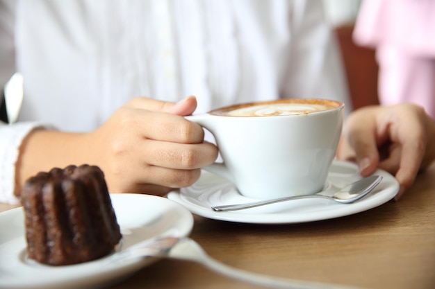 Manos de mujer con café capuchino en una mesa de madera