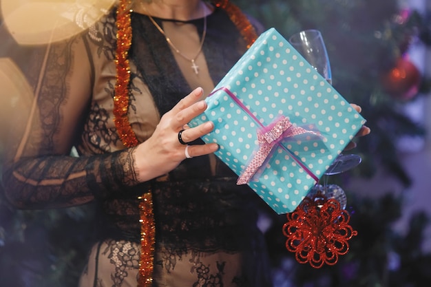 Manos de mujer con una caja de regalo cerca de un árbol de Navidad. Filtro de grano y ruido vintage especial, luces borrosas.