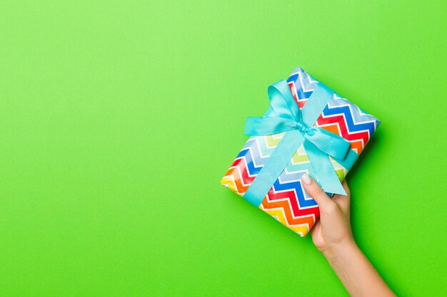 Manos de mujer con caja de regalo sobre fondo de color