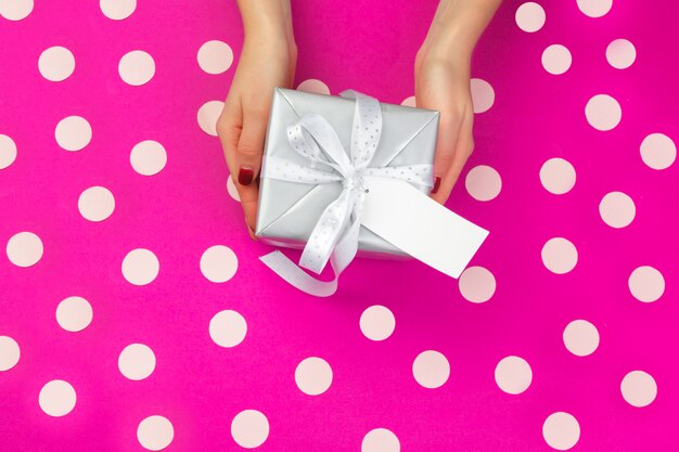 Manos de mujer con caja de regalo sobre fondo rosa