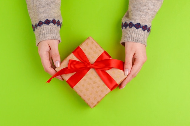 Manos de mujer con caja de regalo sobre fondo verde