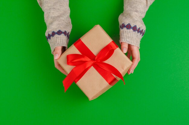 Manos de mujer con caja de regalo sobre fondo verde