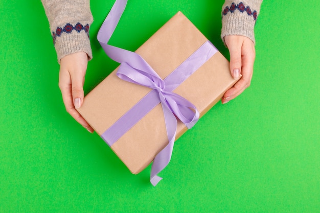 Manos de mujer con caja de regalo sobre fondo verde