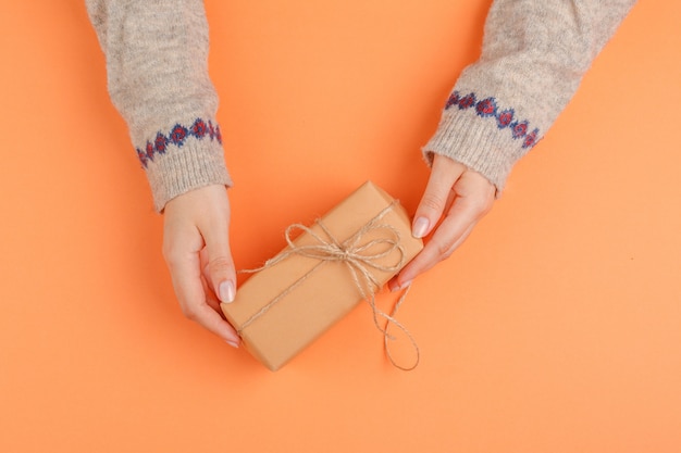 Manos de mujer con caja de regalo en superficie naranja