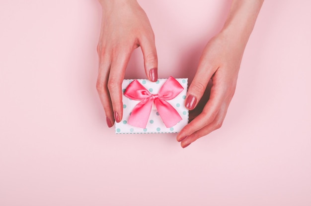 Manos de mujer con caja de regalos en fondo rosa claro