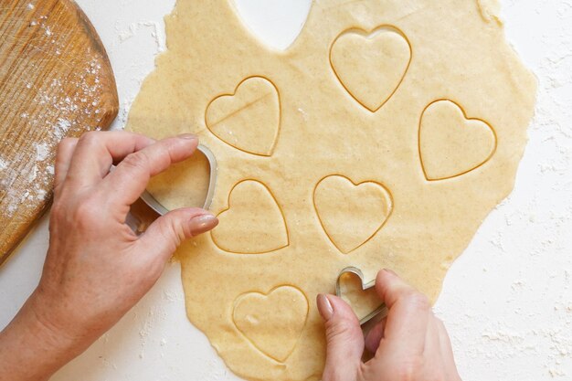 Foto las manos de la mujer cocinando galletas en forma de corazón en la mesa blanca el día de san valentín