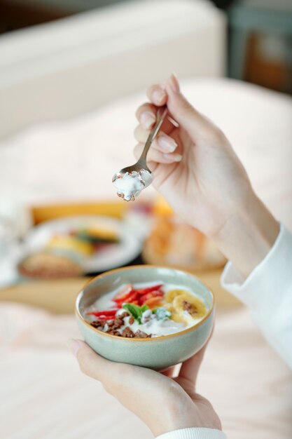 Manos de mujer comiendo granola con rodajas de fruta y yogur no lácteo para el desayuno