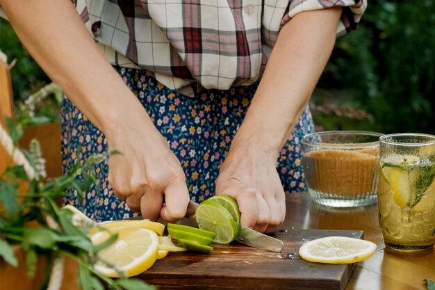 Manos de mujer corta limones y limas para beber limonada de verano