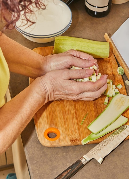 Foto manos de mujer cortadas con un cuchillo en cubos o rodajas de pepino calabacín joven en tabla de cortar de madera. preparación de ingredientes y verduras antes de cocinar