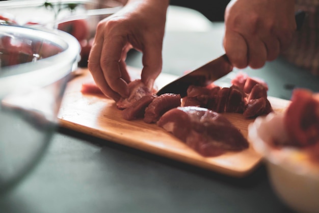 Las manos de la mujer cortan la carne en un tablero de madera b