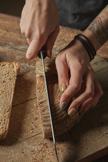 Manos de mujer cortan pan recién horneado sobre una tabla de cortar de madera