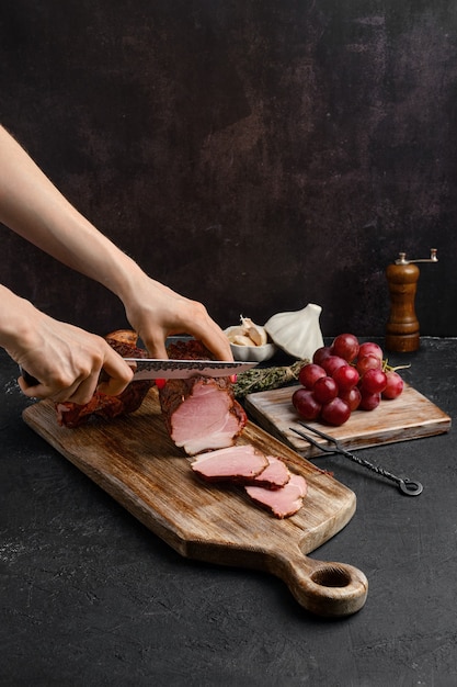 Las manos de una mujer cortan una rebanada de jamón de cerdo secado al aire sobre una tabla de cortar de madera