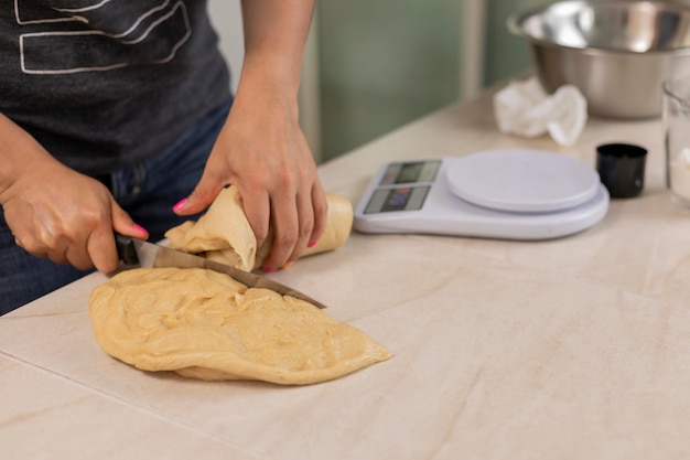 Manos de mujer cortando masa para hacer pan para pesar en una báscula