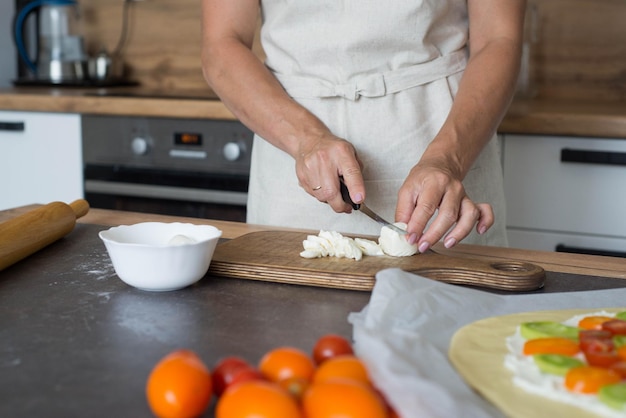 Manos de mujer cortando mozzarella en madera para pizza en la cocina