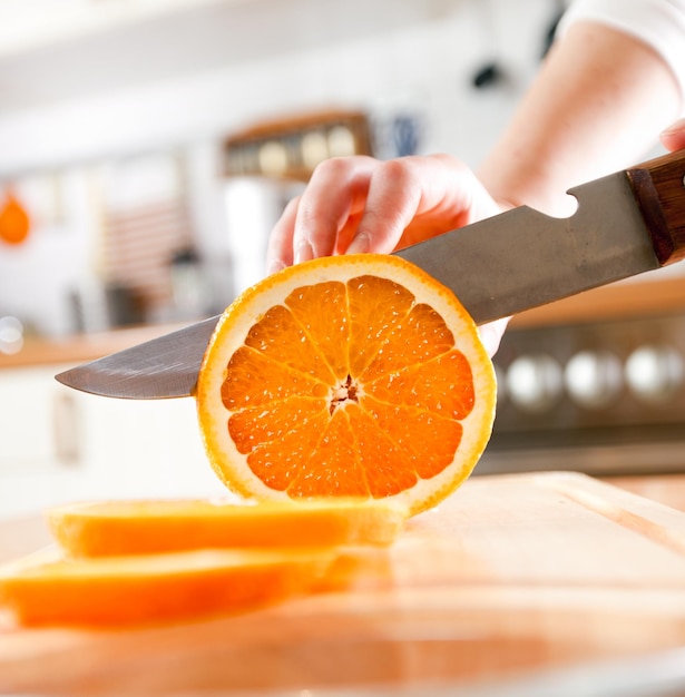 Manos de mujer cortando naranja fresca en la cocina