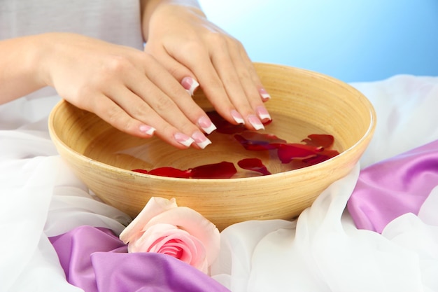 Manos de mujer con cuenco de madera de agua con pétalos sobre fondo azul.