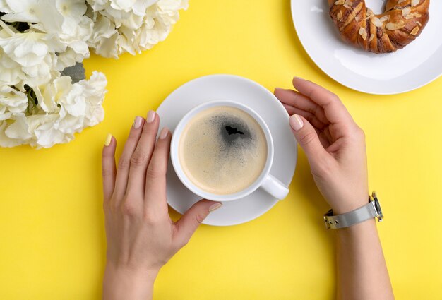 Manos de mujer cuidada sosteniendo una taza de café sobre fondo amarillo