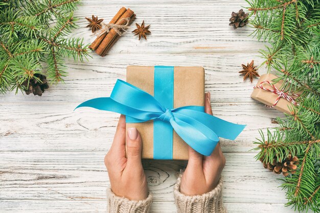 Las manos de la mujer dan el regalo de Navidad hecho a mano envuelto en papel con cinta azul