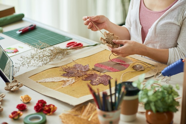 Manos de mujer decorando obras de arte de estilo oshibana con flores hechas de cuerda de lino