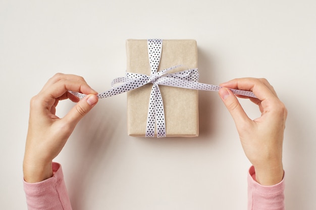 Las manos de la mujer desatan el arco en la caja de regalo en el fondo blanco, visión superior