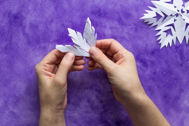 Manos de mujer desplegando papel para revelar copos de nieve en la superficie violeta