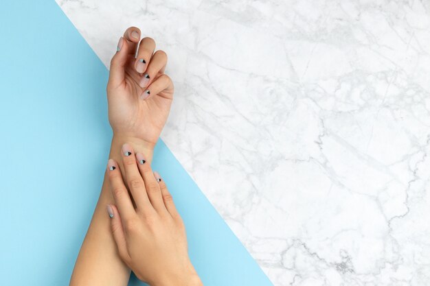 Manos de mujer con diseño de uñas desnudas sobre azul