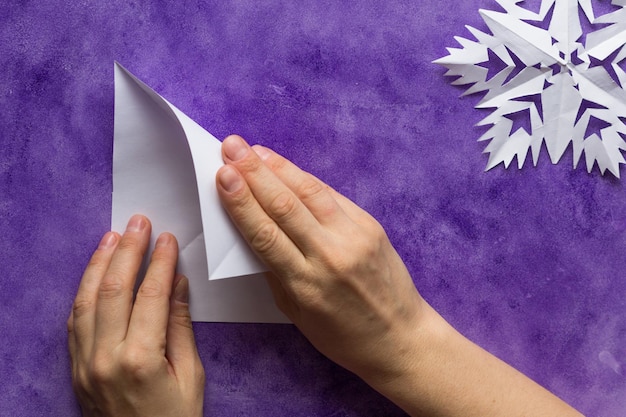 Foto manos de mujer doblando una hoja de papel cuadrada por la mitad para hacer un triángulo en la superficie violeta