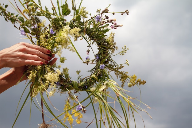 Manos de mujer elaborando la corona de flores silvestres en un cielo azul nublado