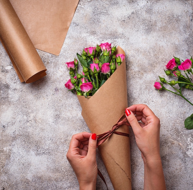 Manos de mujer envuelven un ramo de rosas en papel.