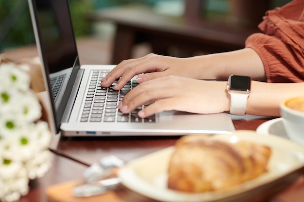 Manos de mujer escribiendo en una laptop cuando escribe artículos para su escuela o sitio web local