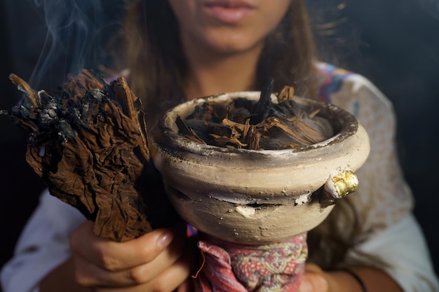 Manos de una mujer espiritual sosteniendo incienso y tabaco quemado