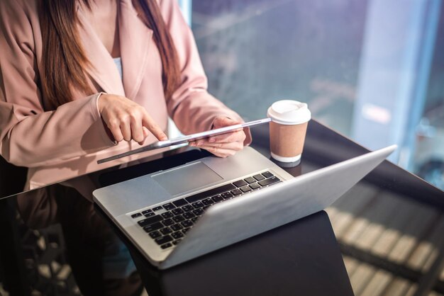 Las manos de la mujer están escribiendo en una computadora portátil y sosteniendo una tableta en la oficina