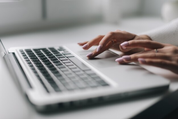 Manos de mujer están escribiendo en el primer plano del teclado de la computadora portátil