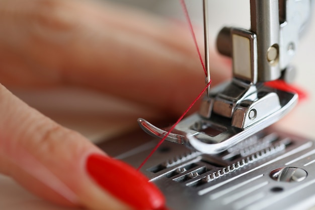 Las manos de la mujer están tirando de un hilo rojo en el servicio de la máquina de coser y trabajan en el equipo