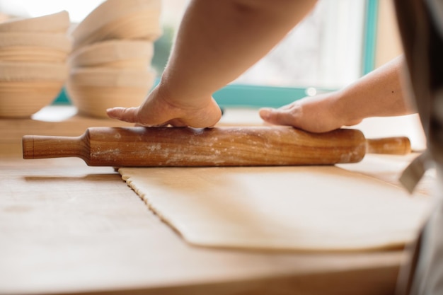 Manos de mujer extendiendo masa en harina con rodillo en panadería