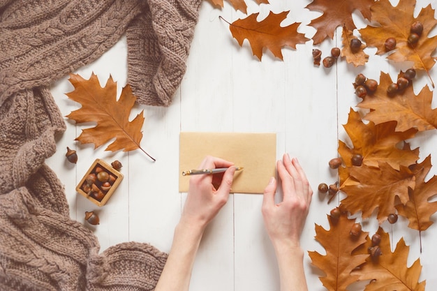 Las manos de la mujer firman un sobre con una tarjeta de felicitación Vista superior Concepto de tiempo de otoño