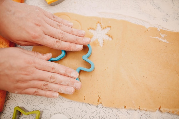 Manos de mujer forman moldes cortadores de masa de jengibre y hacen deliciosas galletas navideñas de jengibre. Cocinar y decorar harina de postre navideña