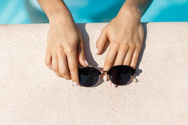 Manos de mujer y gafas de sol en la piscina.