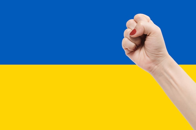 Manos de mujer con gesto de puño en el fondo de color de la bandera de Ucrania