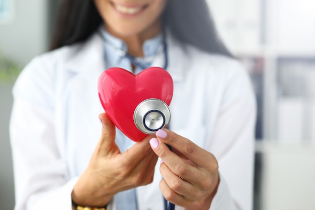 Manos de mujer GP sosteniendo la cabeza del estetoscopio cerca del corazón de juguete rojo