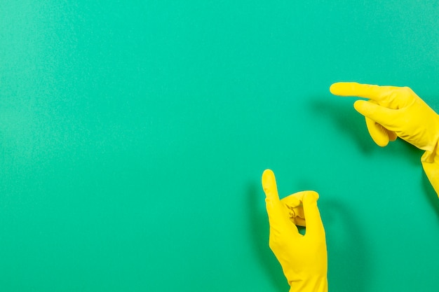 Manos de mujer con guantes de goma amarilla apunta hacia arriba con el dedo, sobre fondo verde