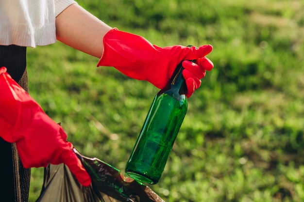 Manos de mujer en guantes de goma roja. Mujer recoge basura en la bolsa. Voluntario recoger basura en el parque de verano. niña recoge botellas de plástico y vidrio en el paquete